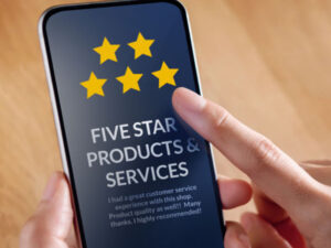 A person is holding a smartphone with their hand and is about to tap the screen. The phone display shows a five-star review with the text "FIVE STAR PRODUCTS & SERVICES" and a positive customer feedback message.