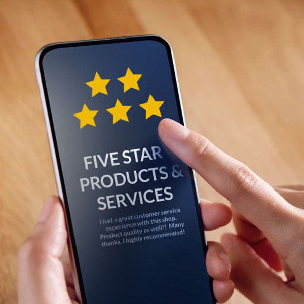 A person is holding a smartphone with their hand and is about to tap the screen. The phone display shows a five-star review with the text "FIVE STAR PRODUCTS & SERVICES" and a positive customer feedback message.