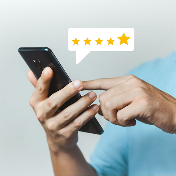 A person wearing a light blue shirt is holding and tapping on a smartphone screen. Above the phone, there is a speech bubble graphic displaying a five-star rating.