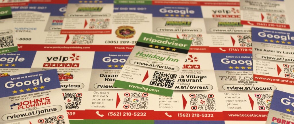 Various business cards and marketing materials scattered over a surface. They include logos for Google, Yelp, and TripAdvisor, with QR codes and contact details for different establishments such as hotels, restaurants, and local services like plumbing. Curious about "How do you ask a customer for a review?